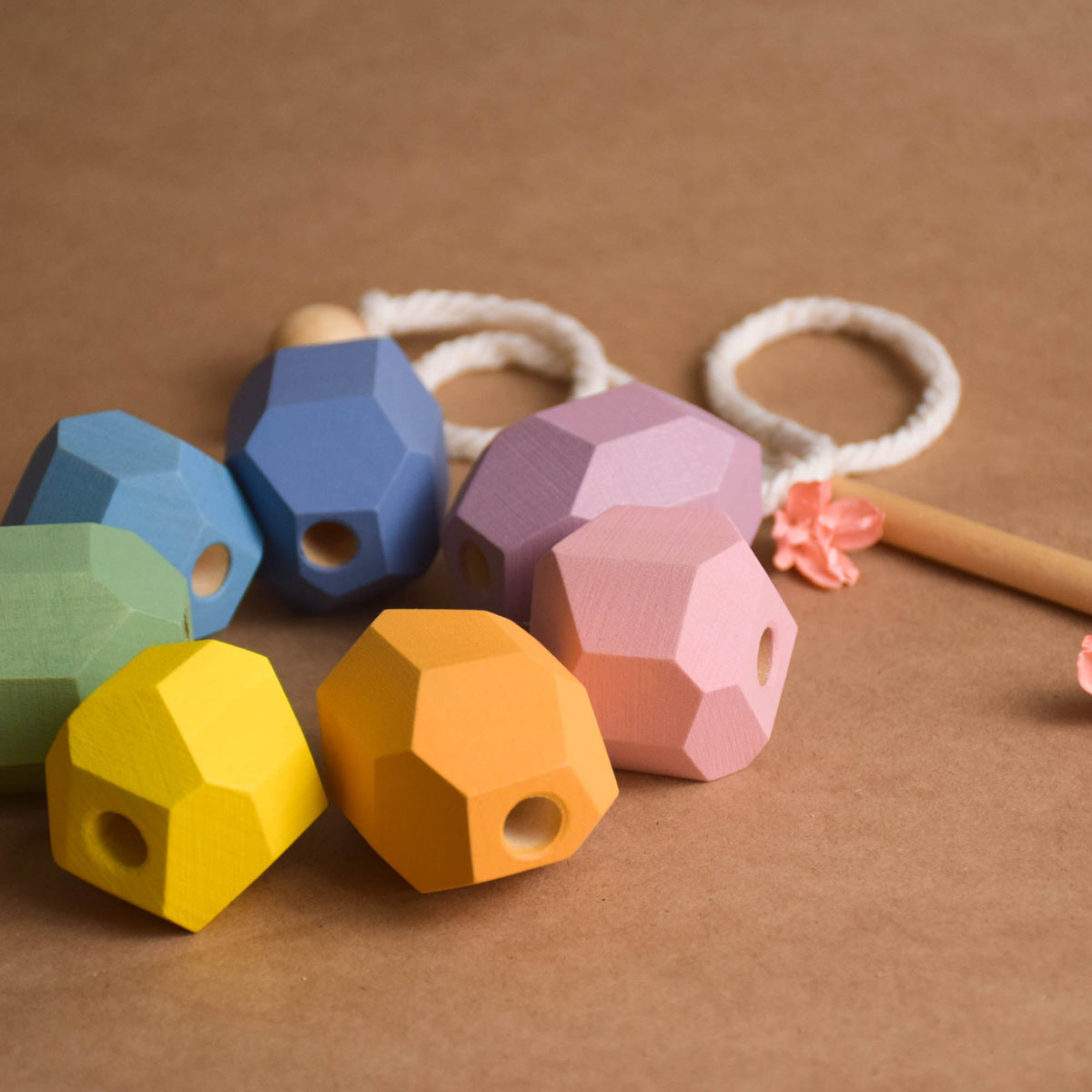Pastel wooden balancing rocks arranged alongside cord as natural landscape elements in open-ended pretend play