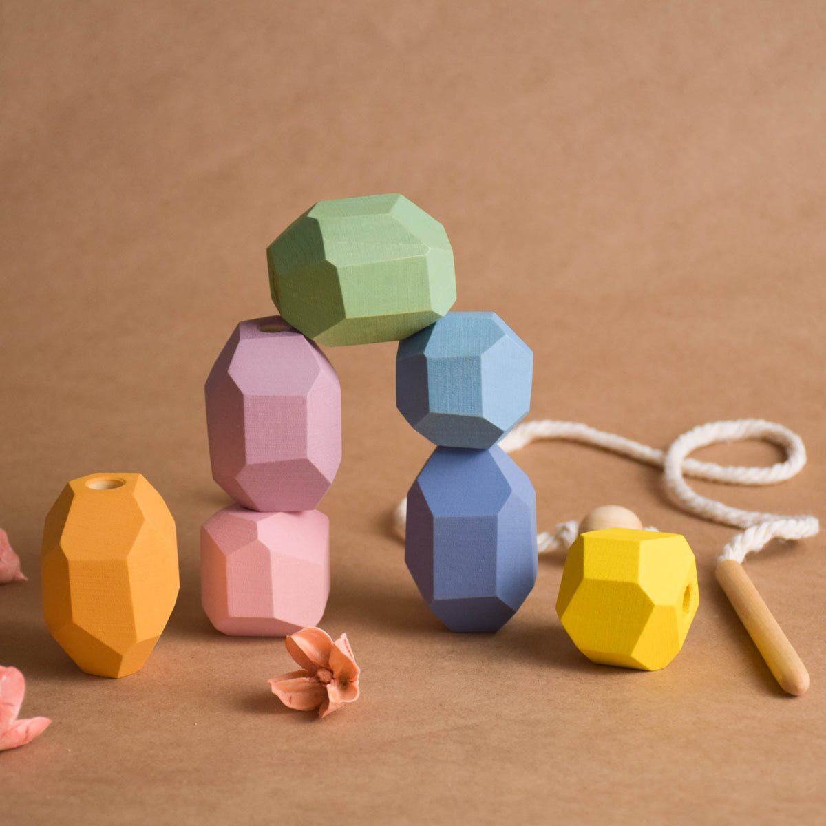 Toddler focused on threading pastel wooden balancing rock with smooth wooden needle for hand-eye coordination training