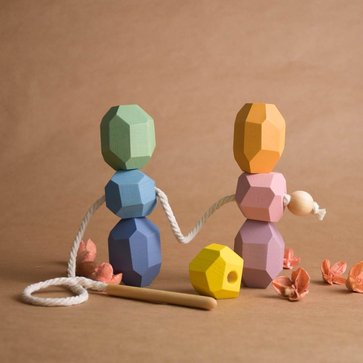 Wooden threading stick passing through faceted pastel linden wood balancing block for fine motor practice