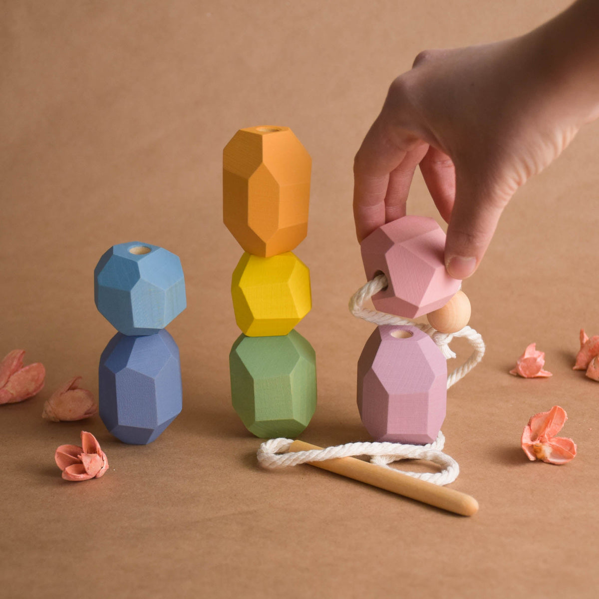 Child hands threading soft pastel wooden balancing blocks onto cord during Montessori-inspired activity