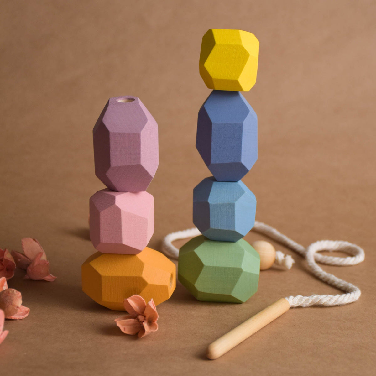 Single faceted pastel wooden lacing stone held in hand showing compact toddler-friendly size and smooth beveled edges