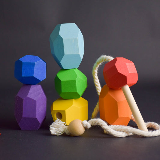 Seven rainbow handmade wooden Tumi Ishi lacing stones with threading stick and twisted cord on white background